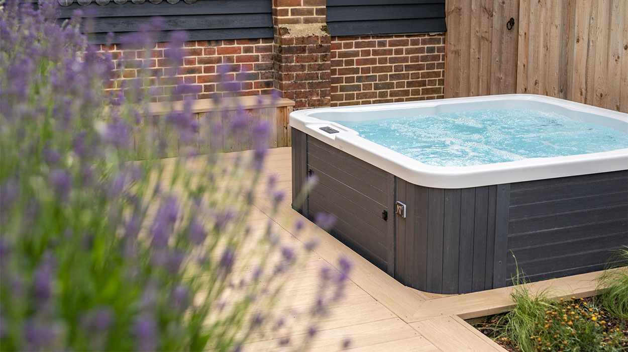 Luxury hot tub outdoors next to a holiday lodge apartment, surrounded by Woodgrain Effect Cedar Wood PVC Decking Boards and plants. Woodgrain Effect PVC Decking provides scratch and water resistance.