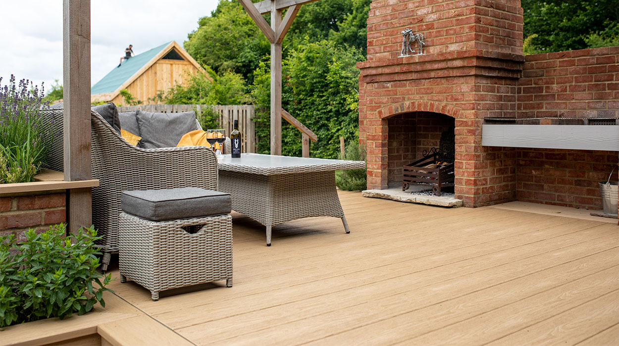 Outdoor BBQ area, including fireplace, table and chairs under a timber veranda, with Cladco Premium PVC Decking in a light Cedar Wood colour. Woodgrain Effect PVC Decking provides scratch and water resistance.
