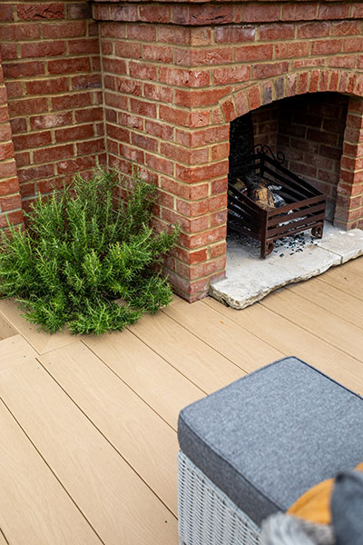 Outdoor fireplace and furniture decorate a patio area, with PVC Decking Boards in Cedar Wood colour featuring a woodgrain effect. Woodgrain Effect PVC Decking provides scratch and water resistance.