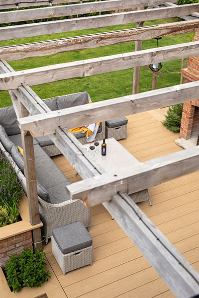 PVC Decking Boards in Cedar Wood colour form this patio decking area outside, underneath a timber veranda. Woodgrain Effect PVC Decking provides scratch and water resistance.