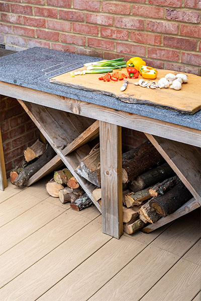 BBQ food on a chopping board and wooden logs above Woodgrain PVC Decking area outdoors. Woodgrain Effect PVC Decking provides scratch and water resistance.