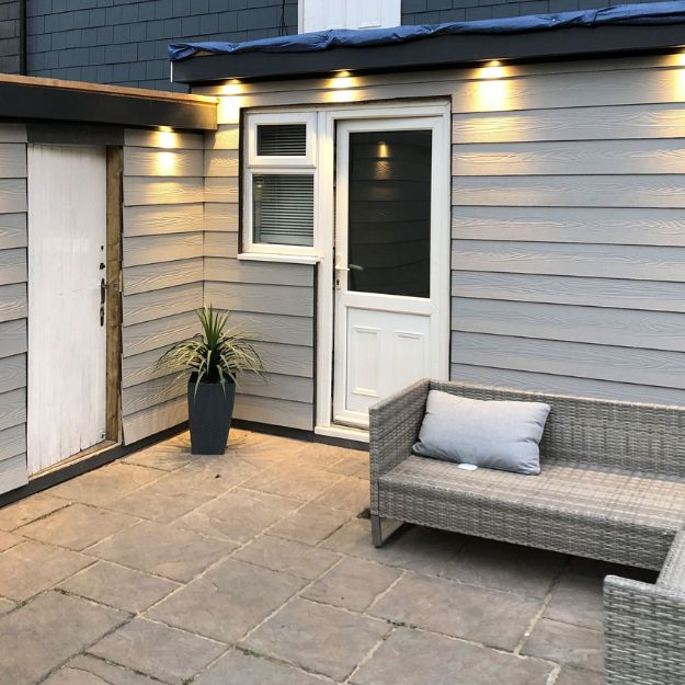 Improve your outside seating space with Fibre Cement Cladding. The Boards give your home a hassle-free, weather-resistant woodgrain aesthetic. Slate-coloured Fibre Cement Boards installed on an outbuilding