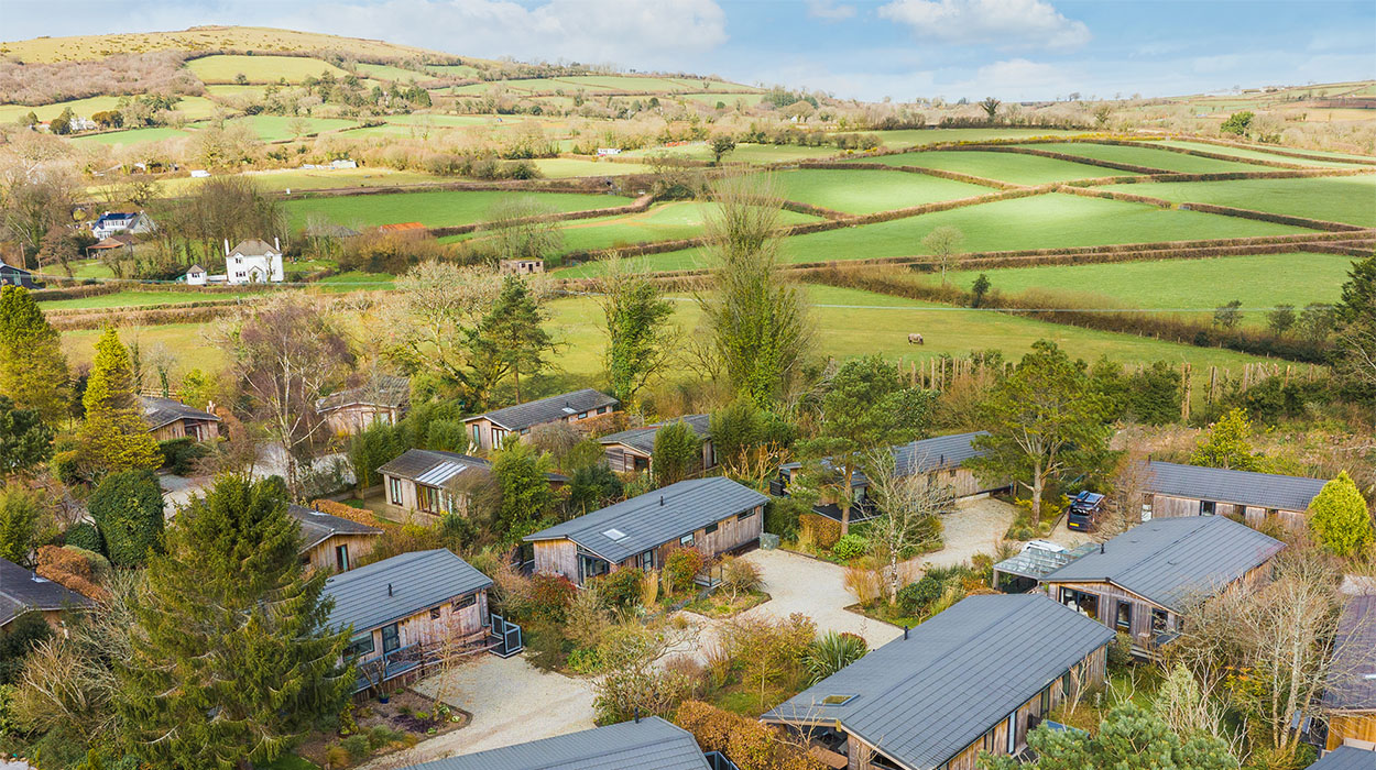 A group of holiday cabins in the countryside overlooking fields and trees.