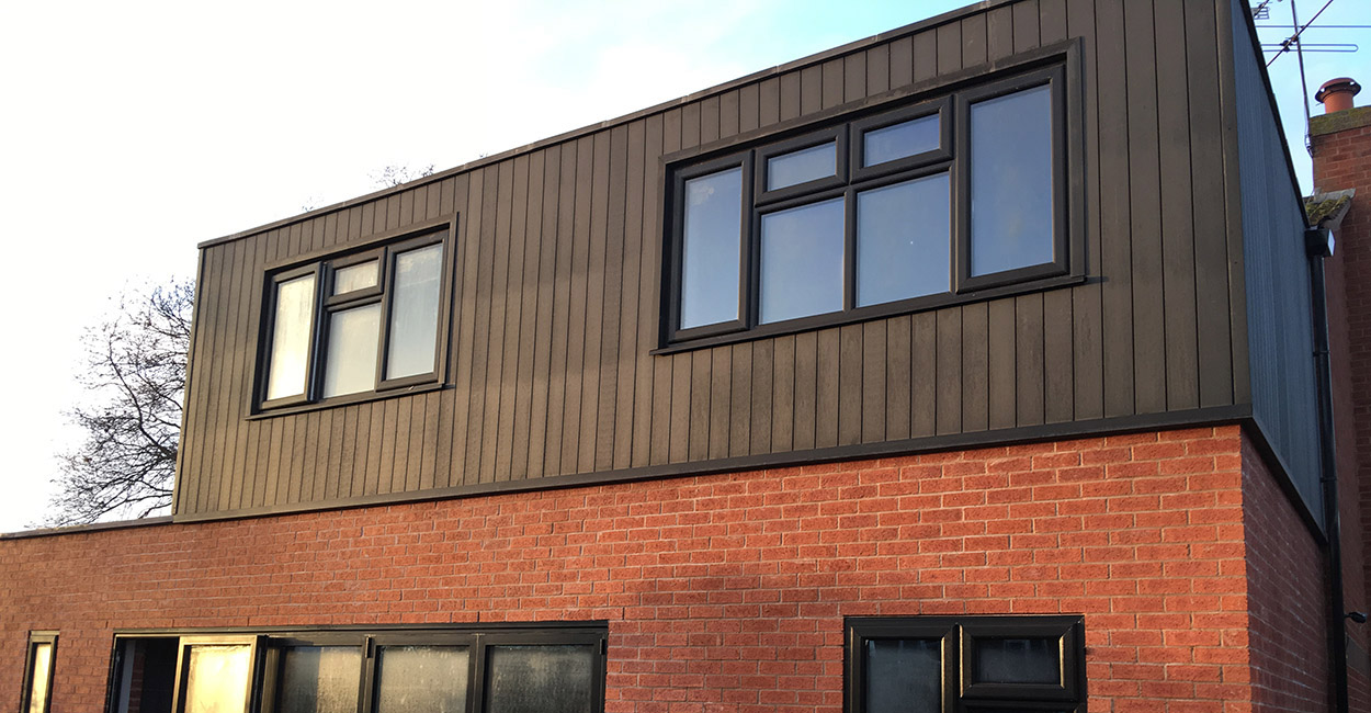 Charcoal Composite Cladding Boards installed vertically on a red brick home