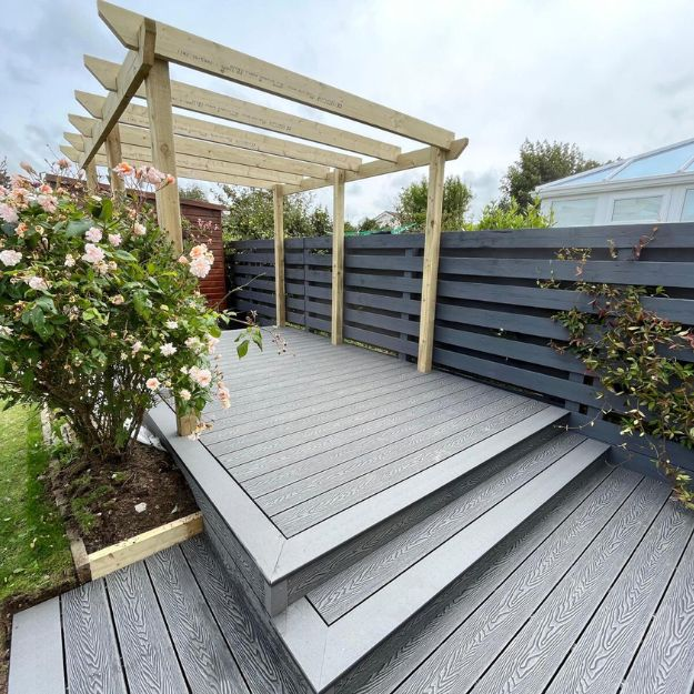 Grey Composite Decking with a wooden pergola frame above it and flowers either side.