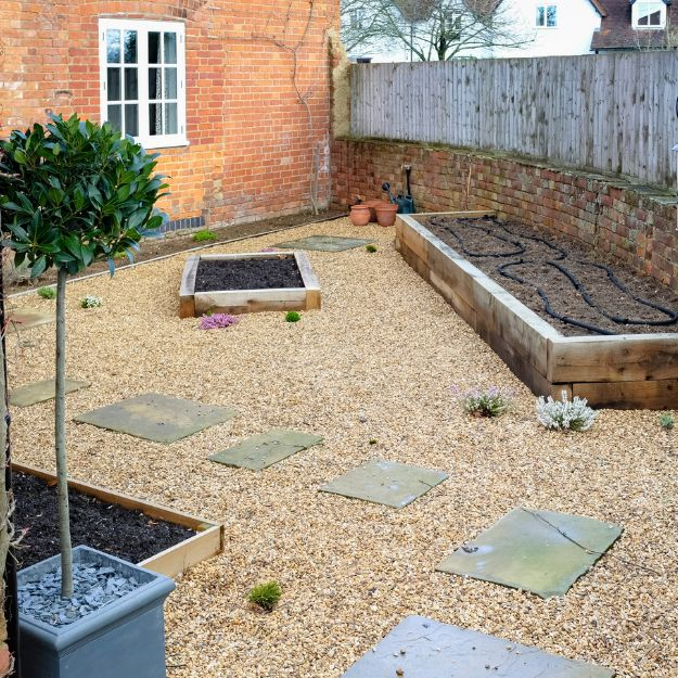 Gravel surface garden with flower beds around the edge and paved stepping stones running down the middle.