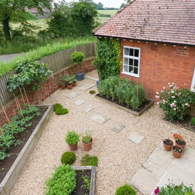 Gravel surface garden with flower beds against a house and walls and stepping stones.