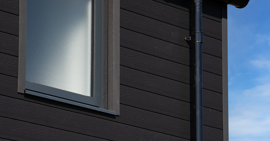 A close up of an upper floor window encased with Cladco Signature composite woodgrain wall cladding in charcoal.